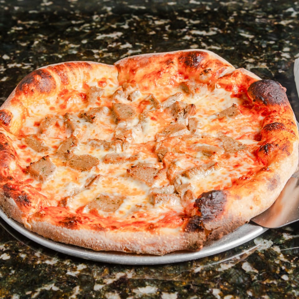 Cheese pizza topped with sliced sausage on a metal serving tray, featuring a thick, charred crust.