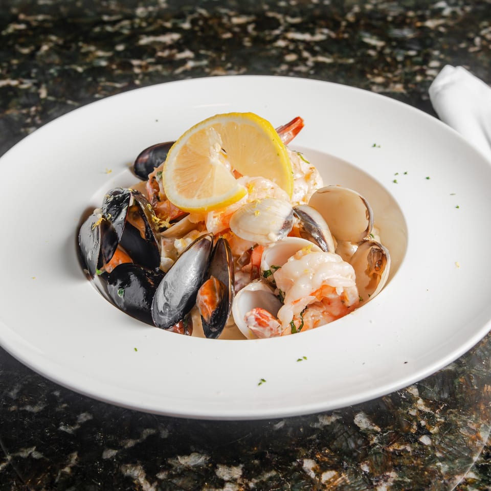 Creamy seafood pasta with shrimp, mussels, clams, and lemon slices served on a white plate.