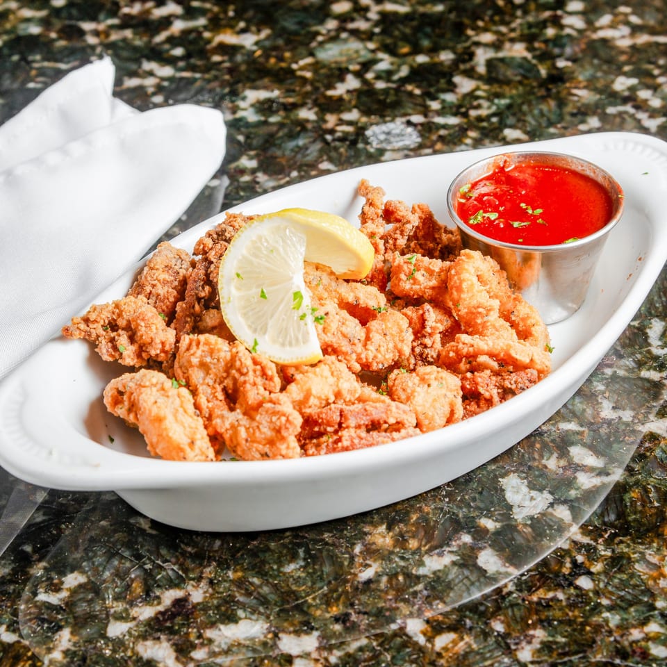 Crispy fried seafood topped with lemon slices and parsley, served with red dipping sauce on a white platter.