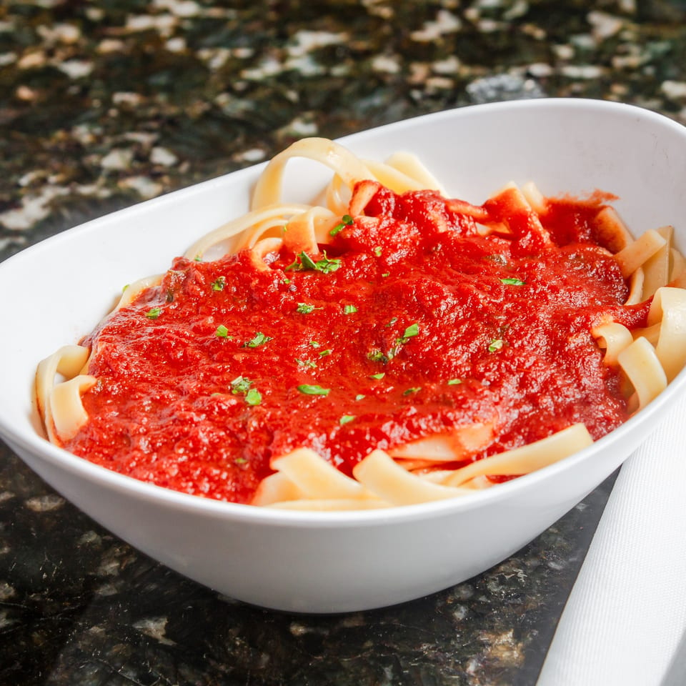 Pasta topped with chunky red tomato sauce and fresh herbs in a white bowl on a granite countertop.